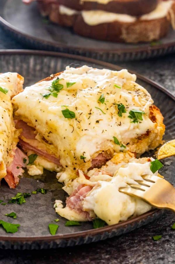 a croque monsieur sandwich on a plate cut in a half with a fork holding a bite.