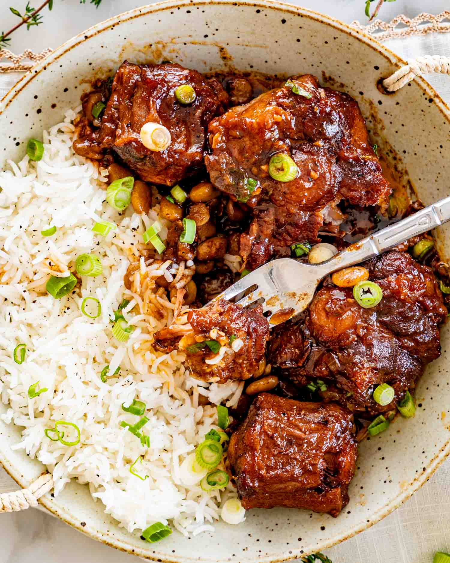 Tender oxtail served over white rice with lima beans, glossy sauce coating meat, fork pulling apart fall off bone pieces.