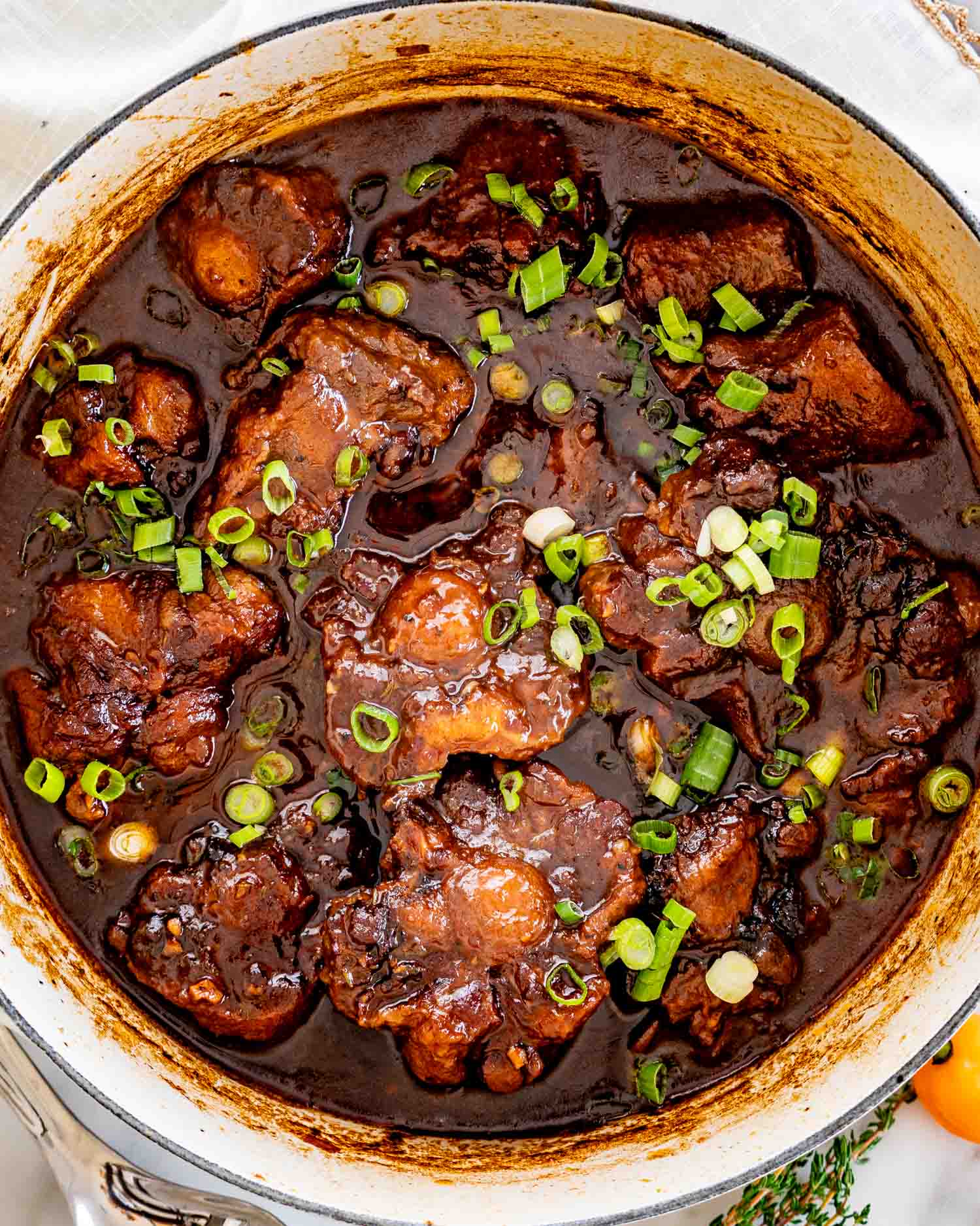 Rich Jamaican oxtail stew simmering in a pot, glossy dark sauce with tender beef pieces and fresh green onions on top.