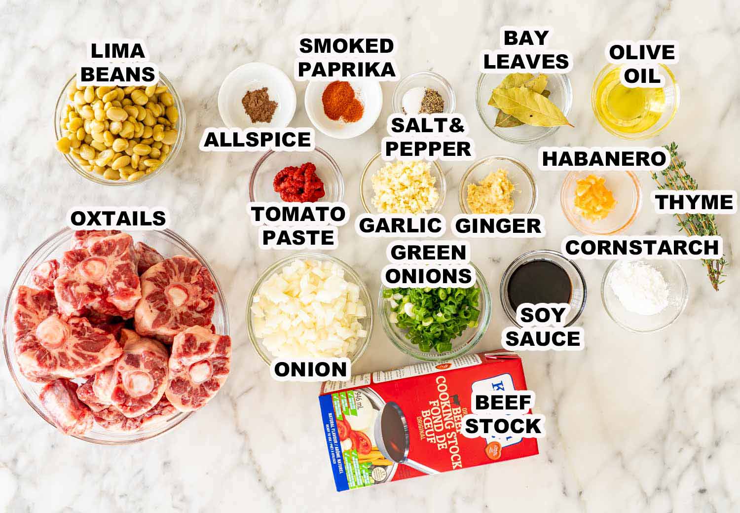 Raw oxtails, lima beans, spices, garlic, ginger, and beef broth arranged neatly for Jamaican style oxtail stew preparation.