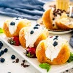 3 rum babas on a white platter topped with whipped cream and berries.