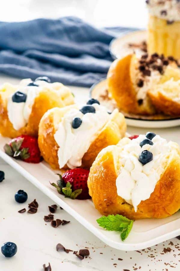 3 rum babas on a white platter topped with whipped cream and berries.