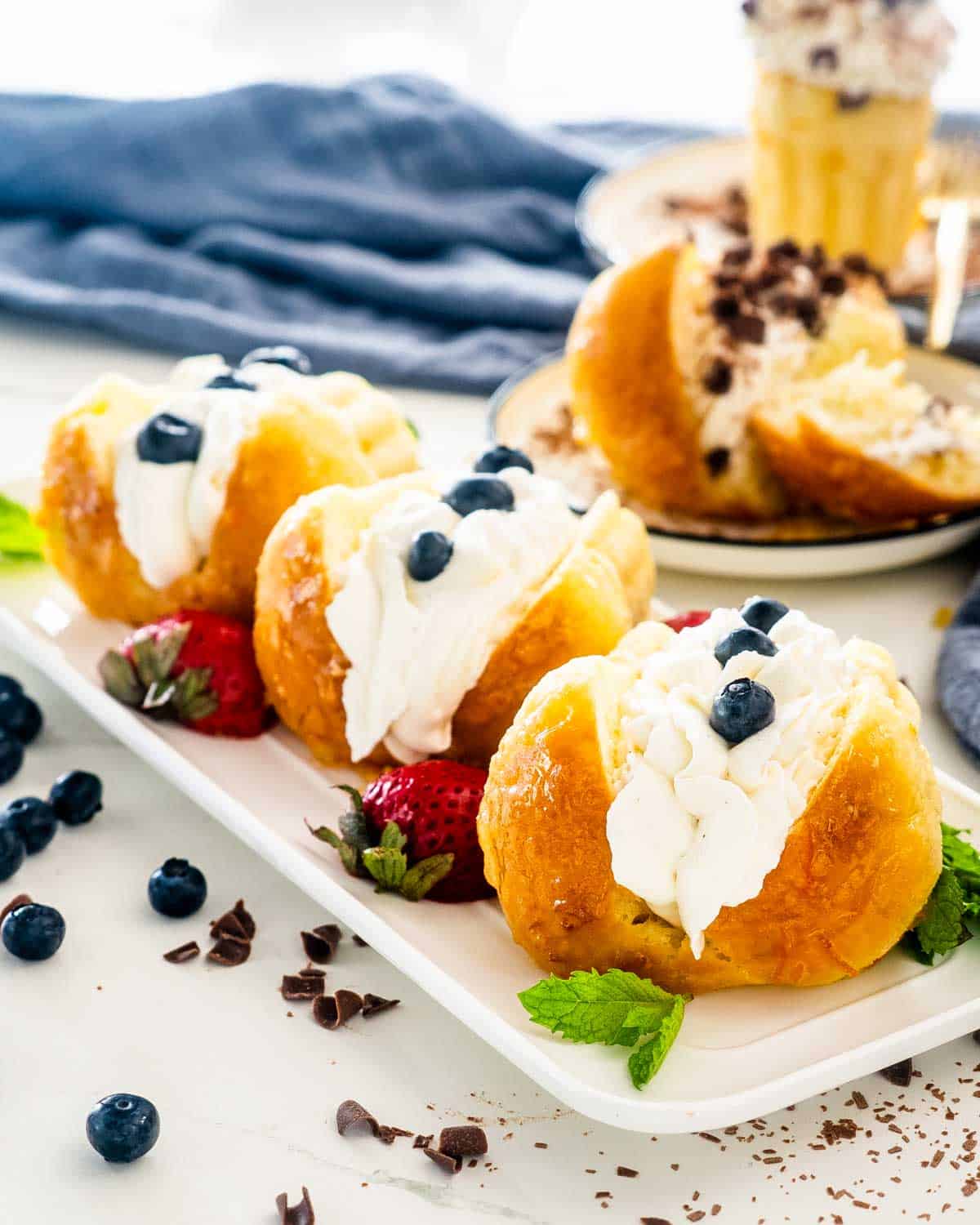 3 rum babas on a white platter topped with whipped cream and berries.