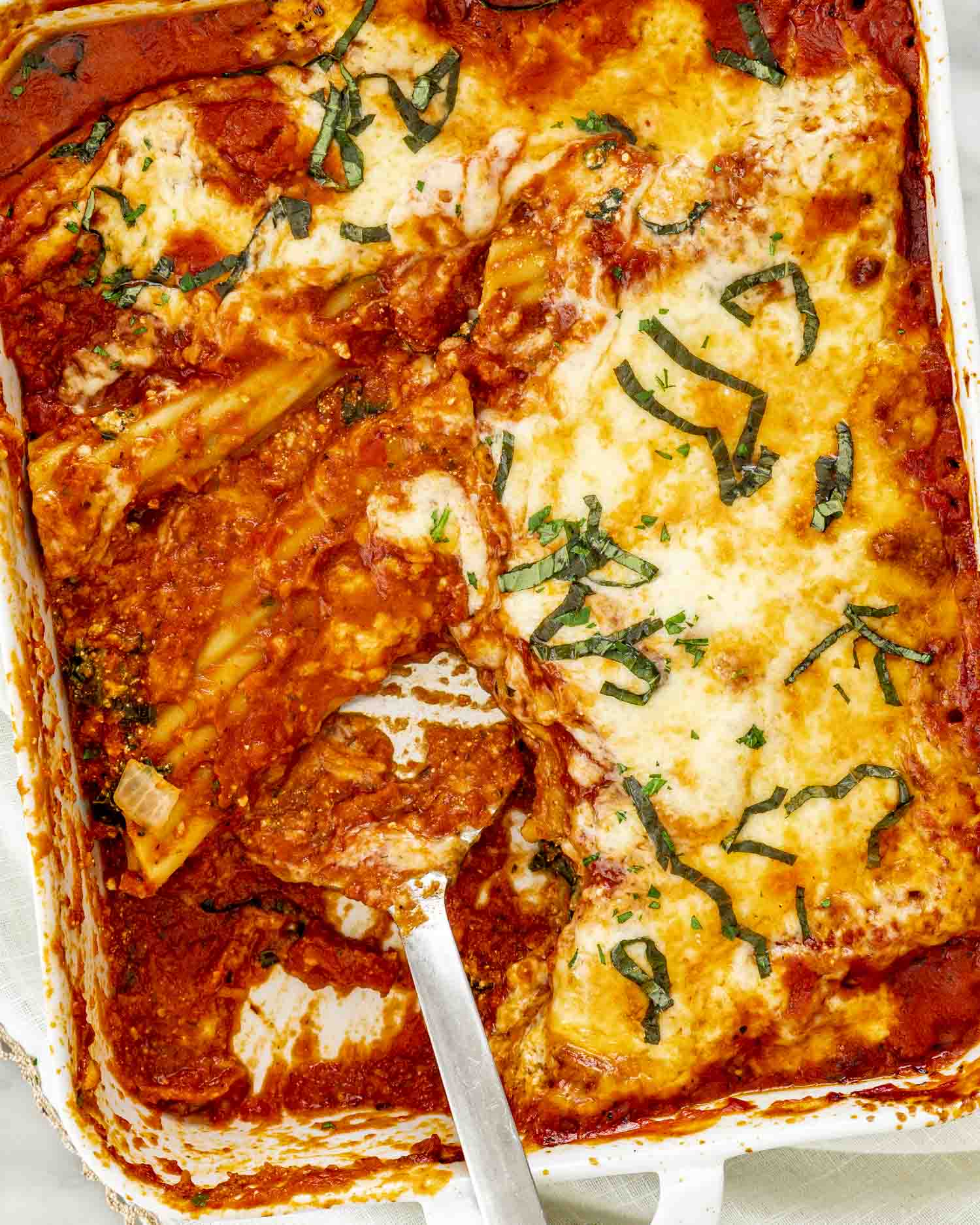 stuffed manicotti being lifted from the pan.