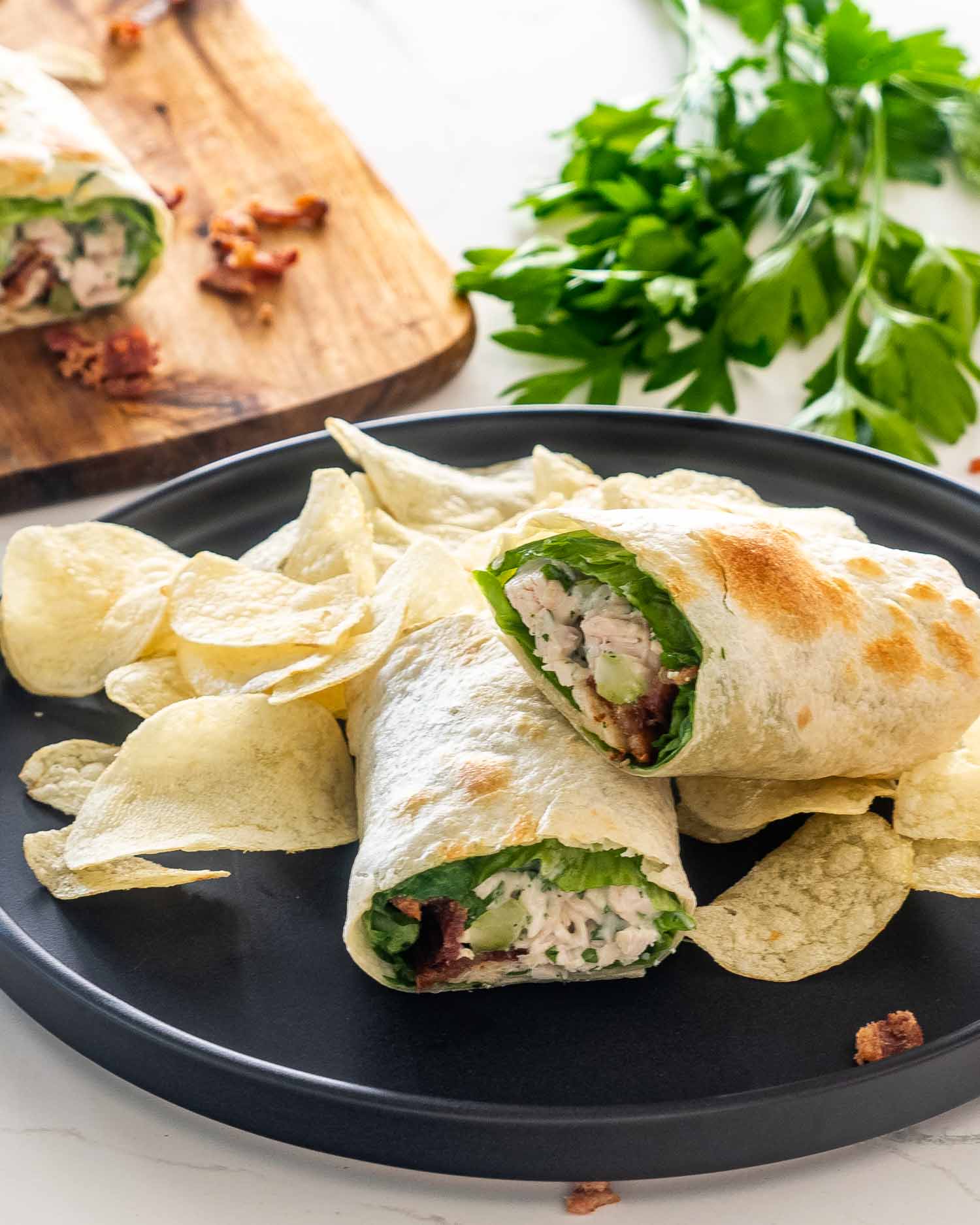 chicken bacon ranch wraps on a black plate with potato chips.