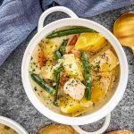 chicken stew in a white bowl next to a couple slices of bread.