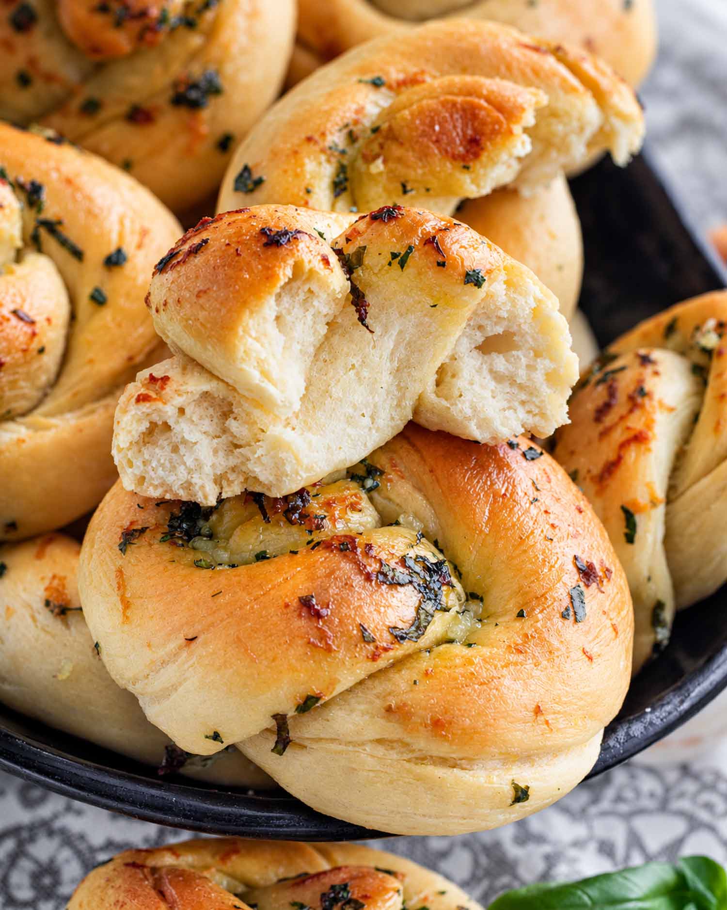 Torn garlic knot revealing its fluffy interior, resting on golden knots brushed with butter and sprinkled with garlic and herbs.