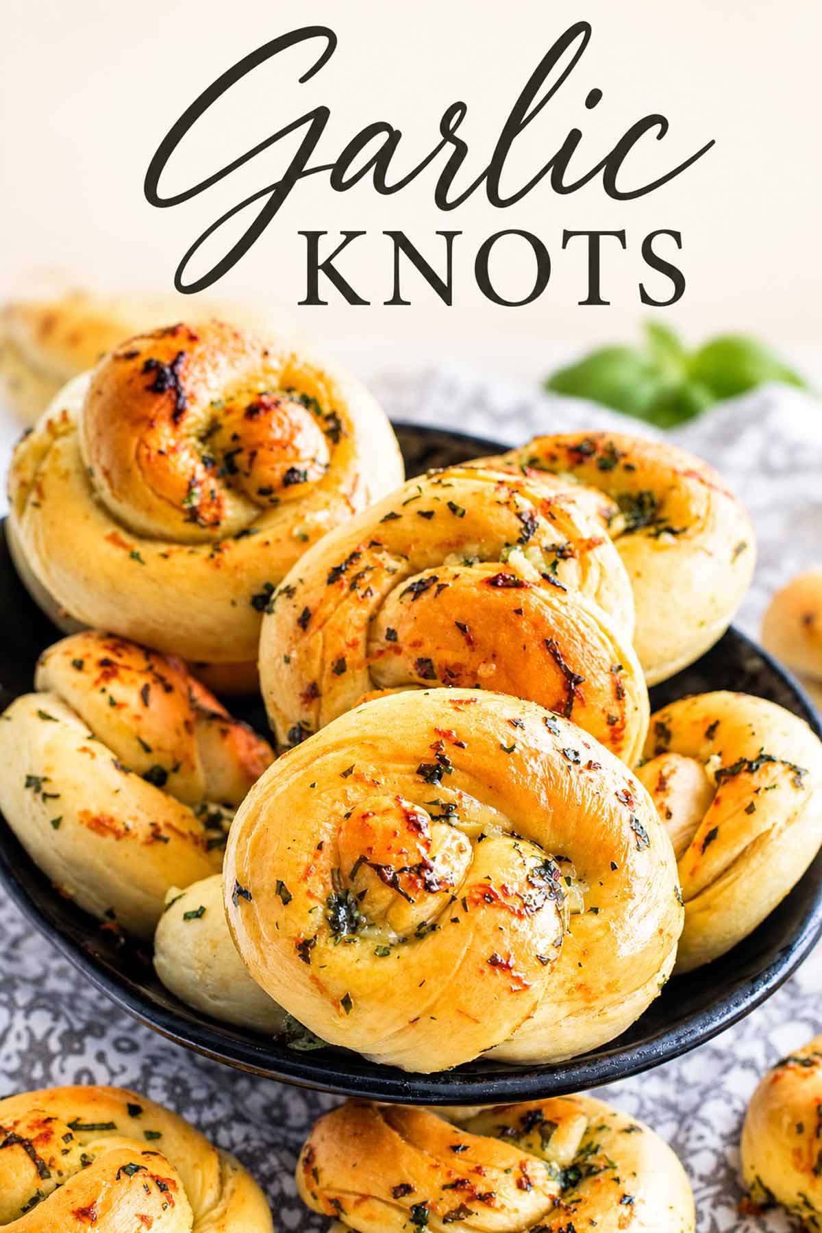 Golden garlic knots sprinkled with herbs piled in a black bowl, with “Garlic Knots” in elegant lettering at the top.