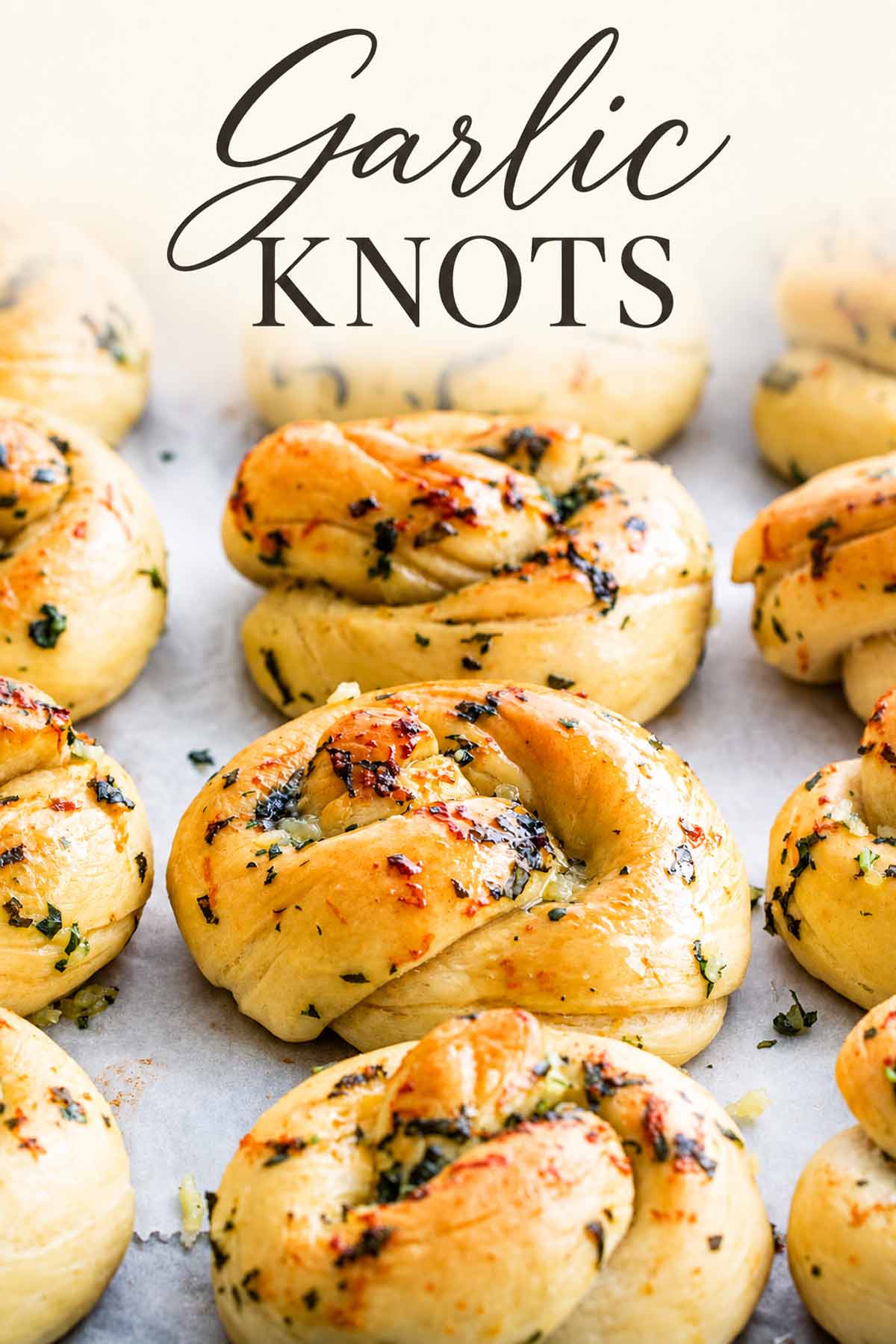 Golden garlic knots topped with chopped herbs arranged on parchment paper, with “Garlic Knots” in script and serif lettering above.