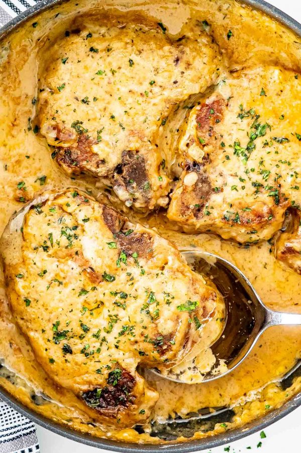 smothered pork chops in a skillet garnished with parsley.