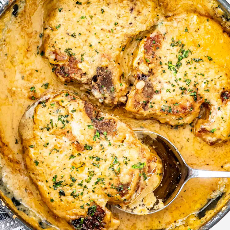 smothered pork chops in a skillet garnished with parsley.