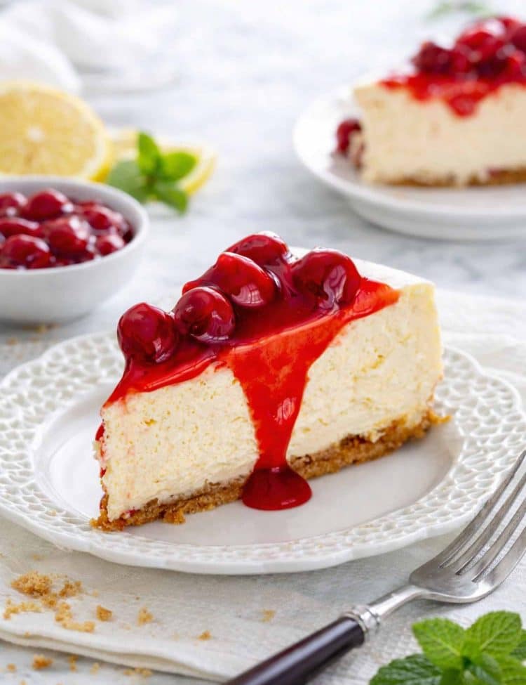 a cheesecake slice with cherry topping on a plate with a fork.