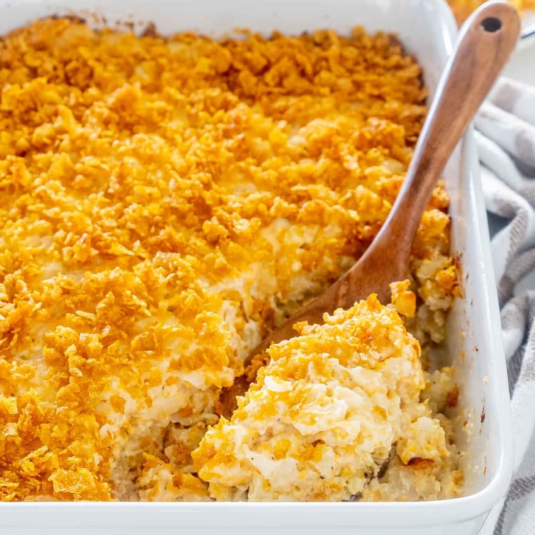 funeral potatoes freshly baked in a casserole dish with a wooden serving spoon inside.