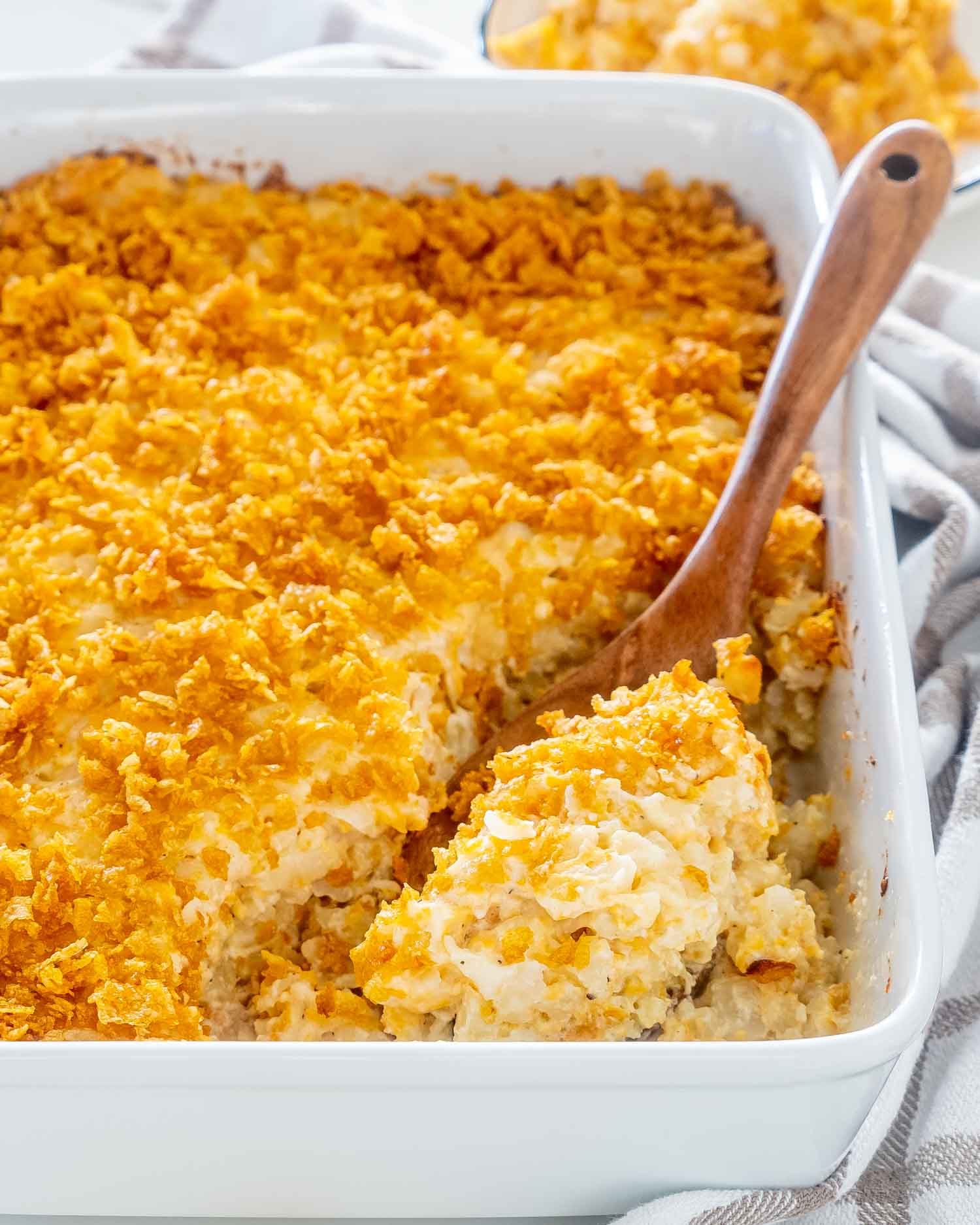 funeral potatoes freshly baked in a casserole dish with a wooden serving spoon inside.