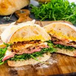 a homemade steak sandwich cut in half on a cutting board.