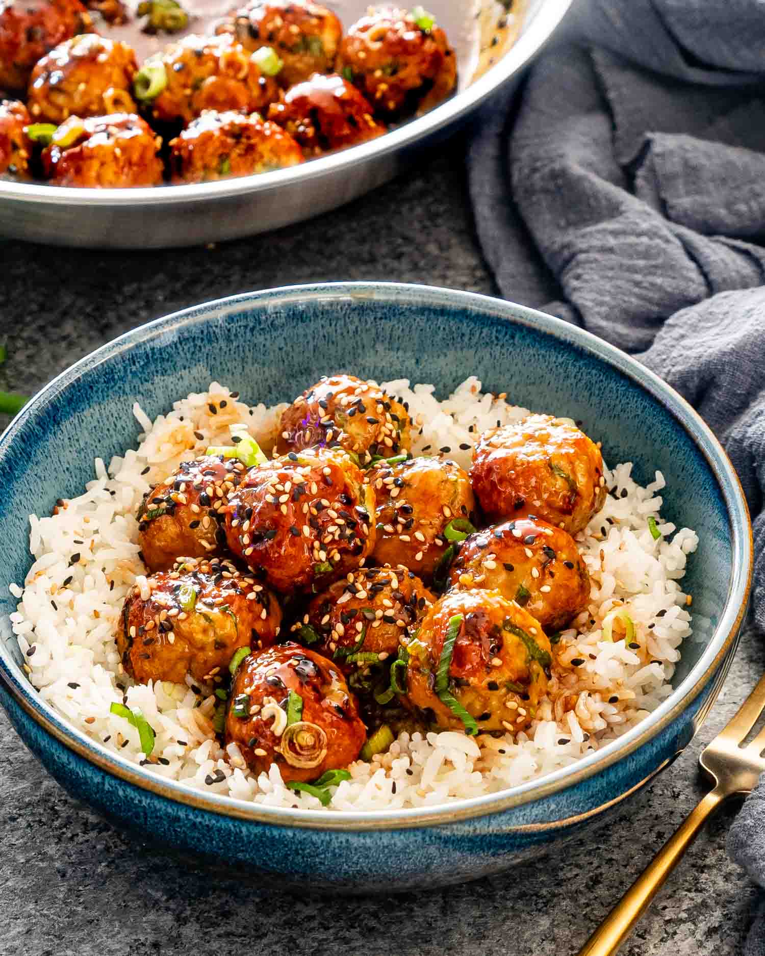teriyaki chicken meatballs over a bed of rice in a blue bowl garnished with green onions.