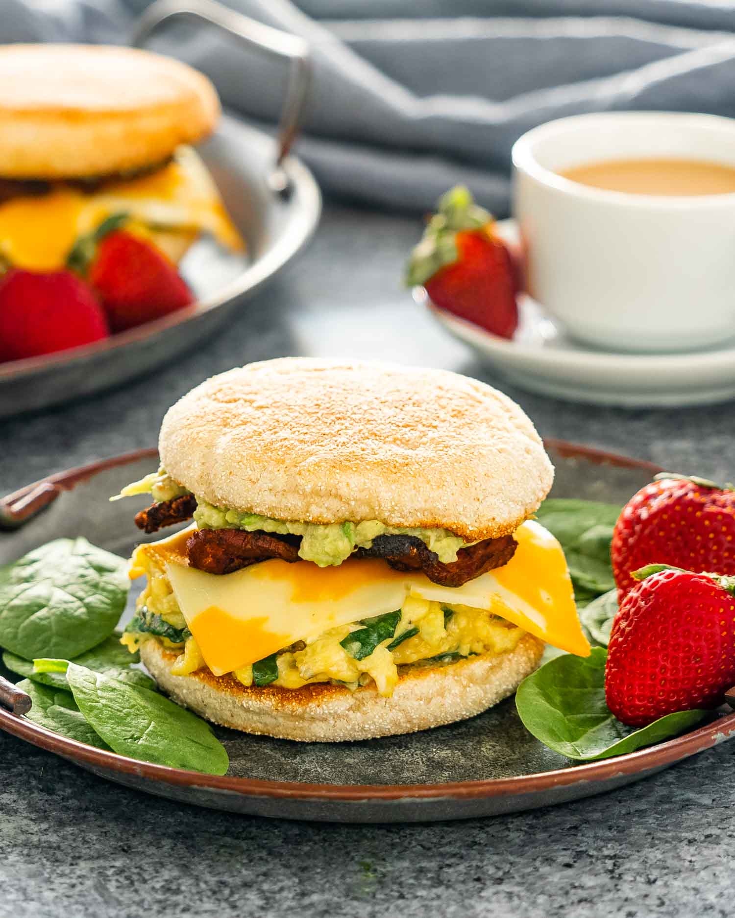 a breakfast sandwich on a metal plate with strawberries on the side.