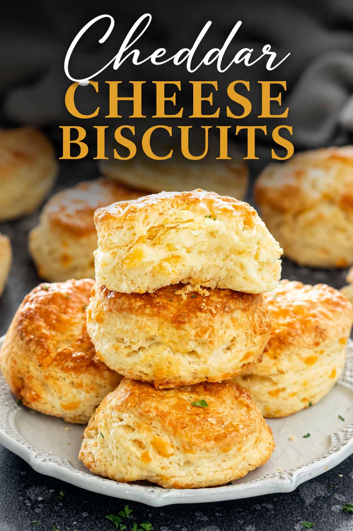 Flaky cheddar cheese biscuits stacked on a plate with golden tops and a cheddar cheese biscuits title overlay.