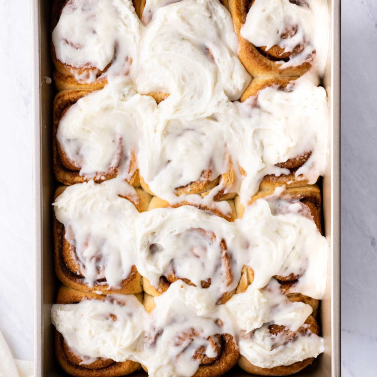 freshly baked cinnabon cinnamon rolls in a baking dish with cream cheese icing.
