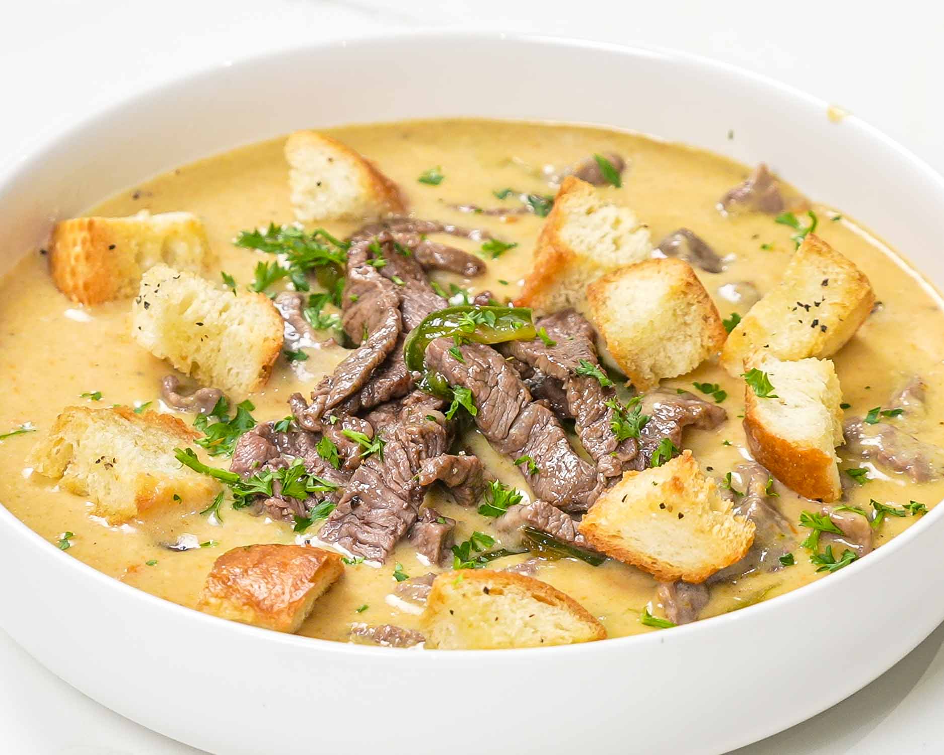philly cheesesteak soup in a white bowl topped with croutons.