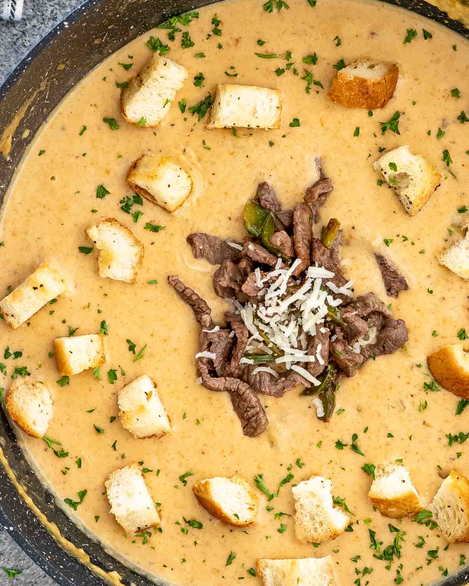 philly cheesesteak soup in a soup pot topped with beef and croutons.