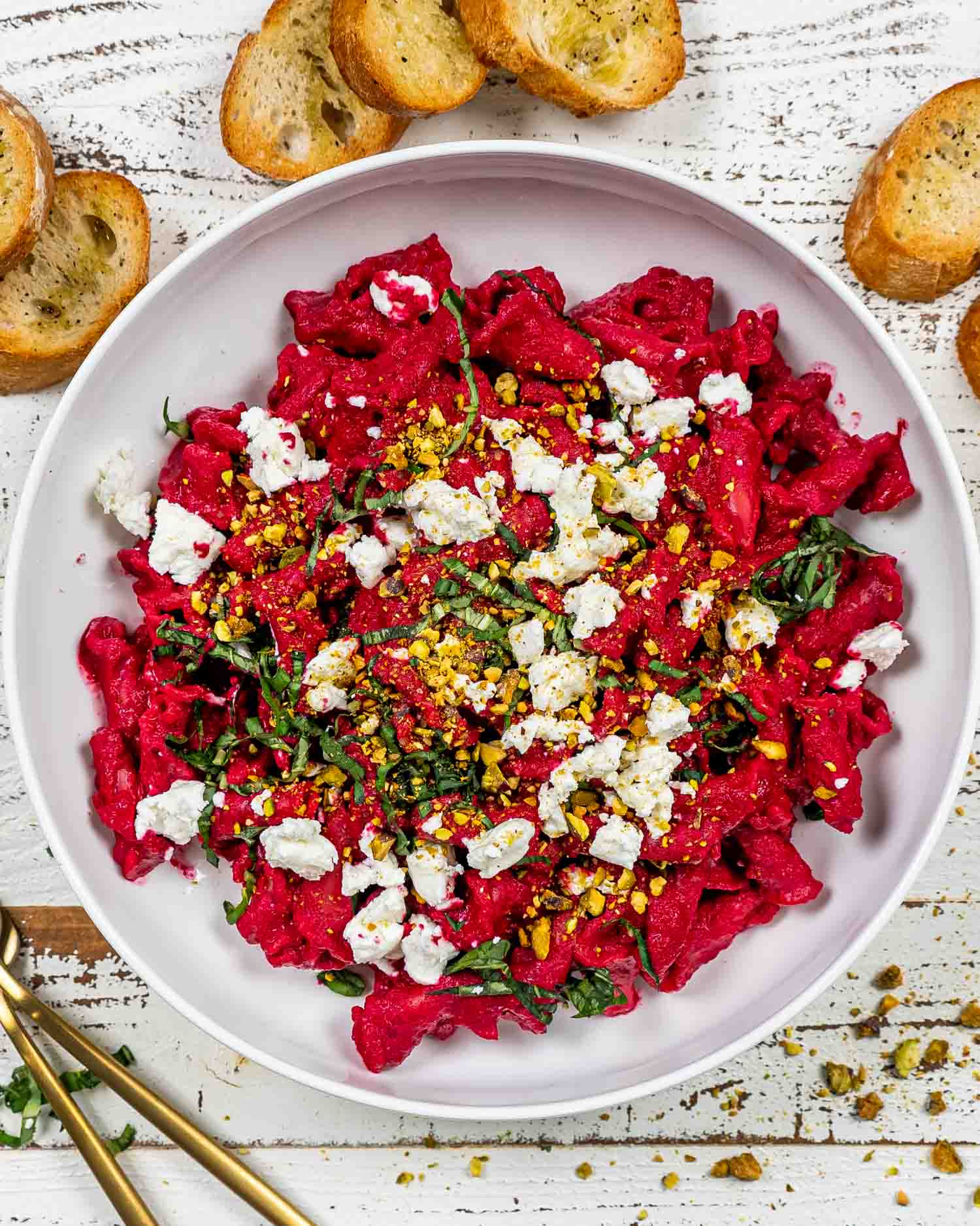 beets and goat cheese pasta on a white plate garnished with goat cheese, basil and pistachios.
