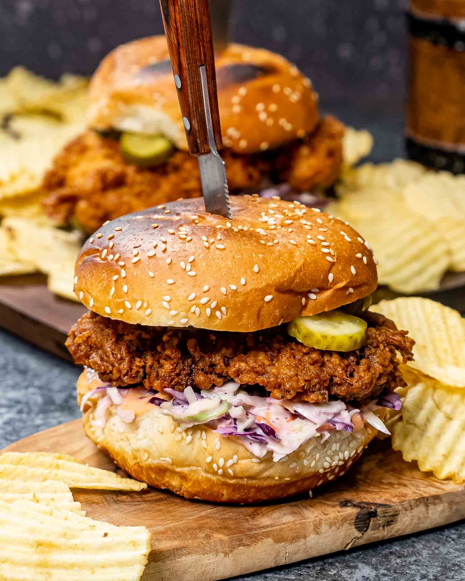 a crispy fried chicken sandwich with coleslaw on a cutting board with potato chips.