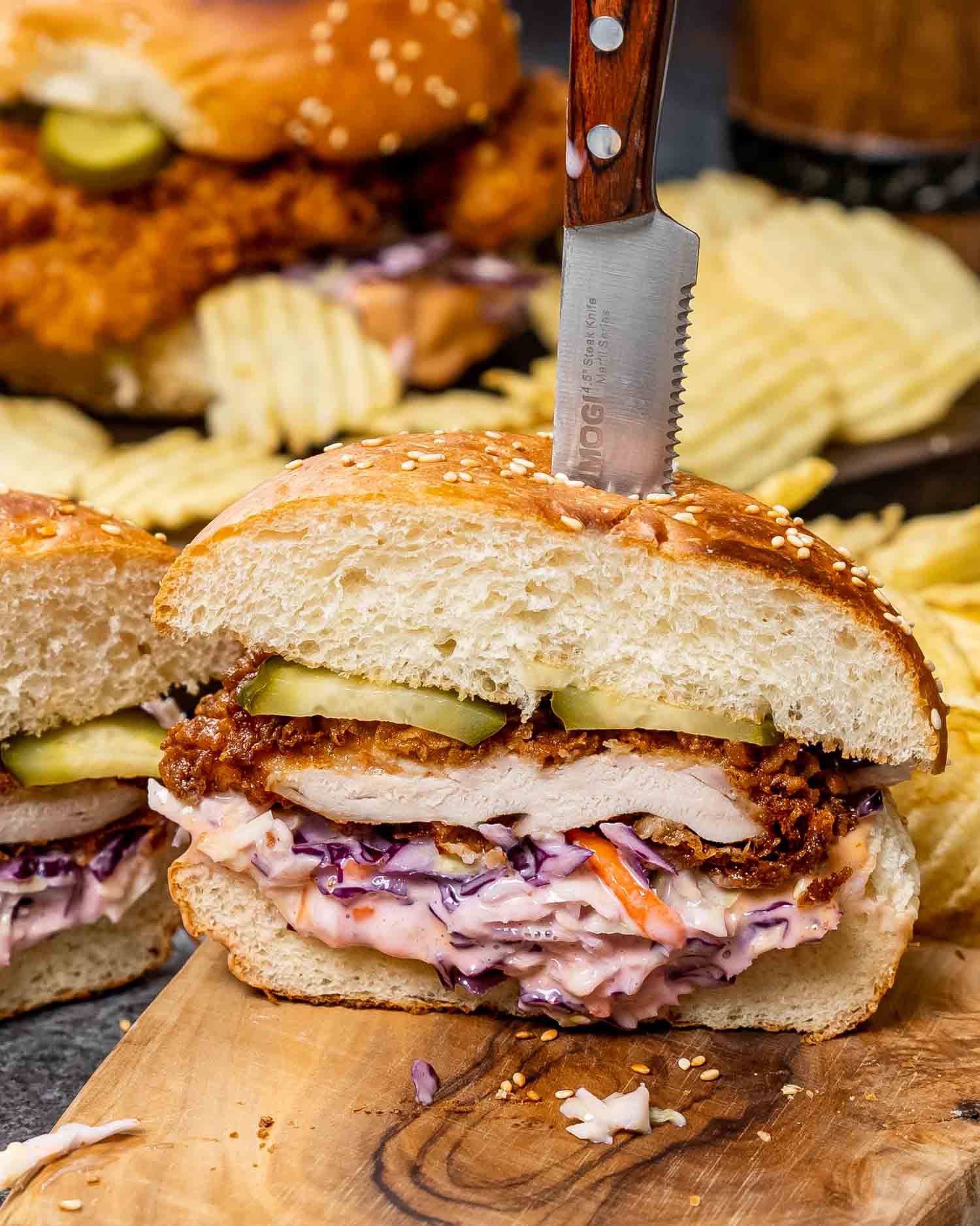 a crispy fried chicken sandwich cut in half with coleslaw on a cutting board with potato chips.