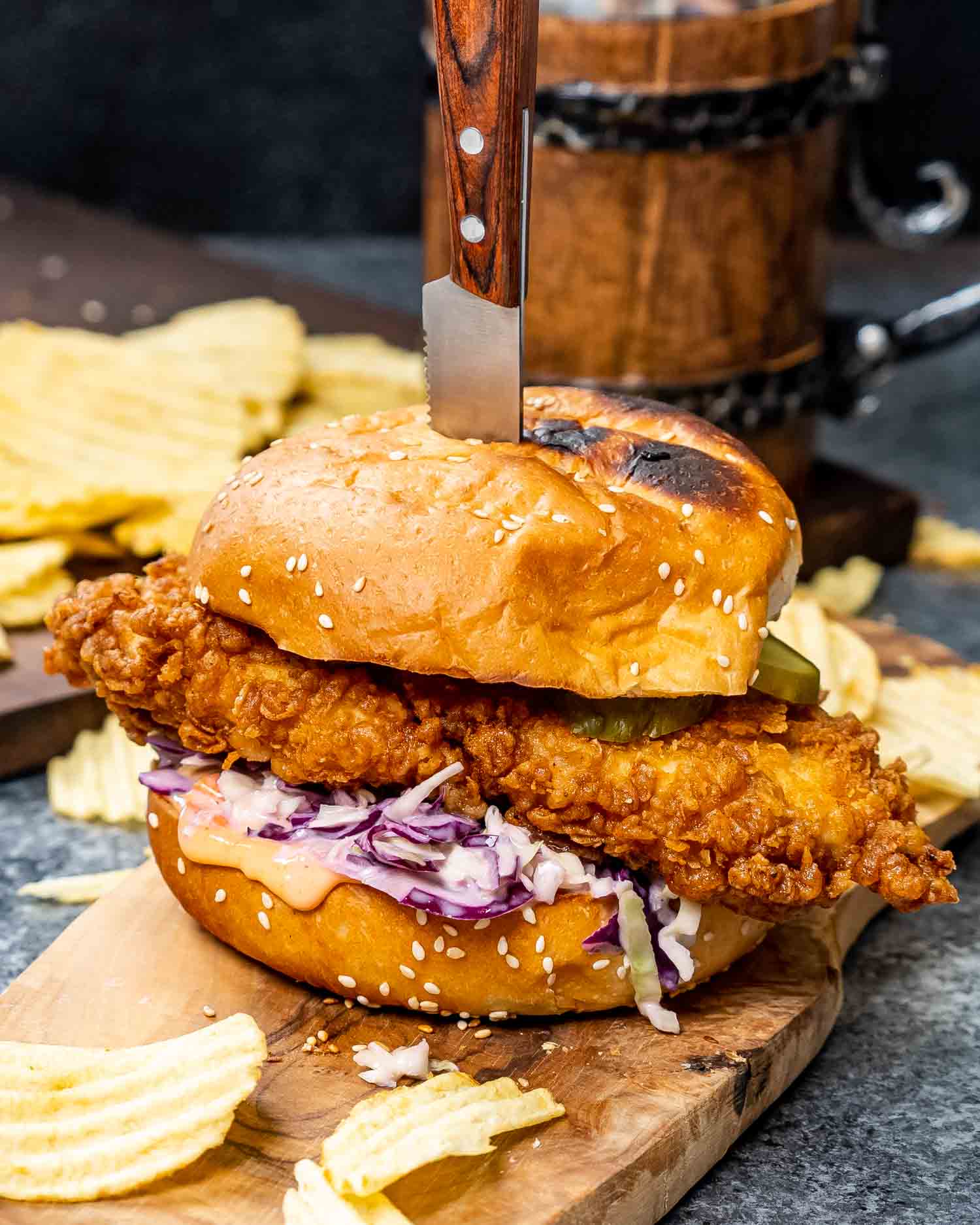 a crispy fried chicken sandwich with coleslaw on a cutting board with potato chips.