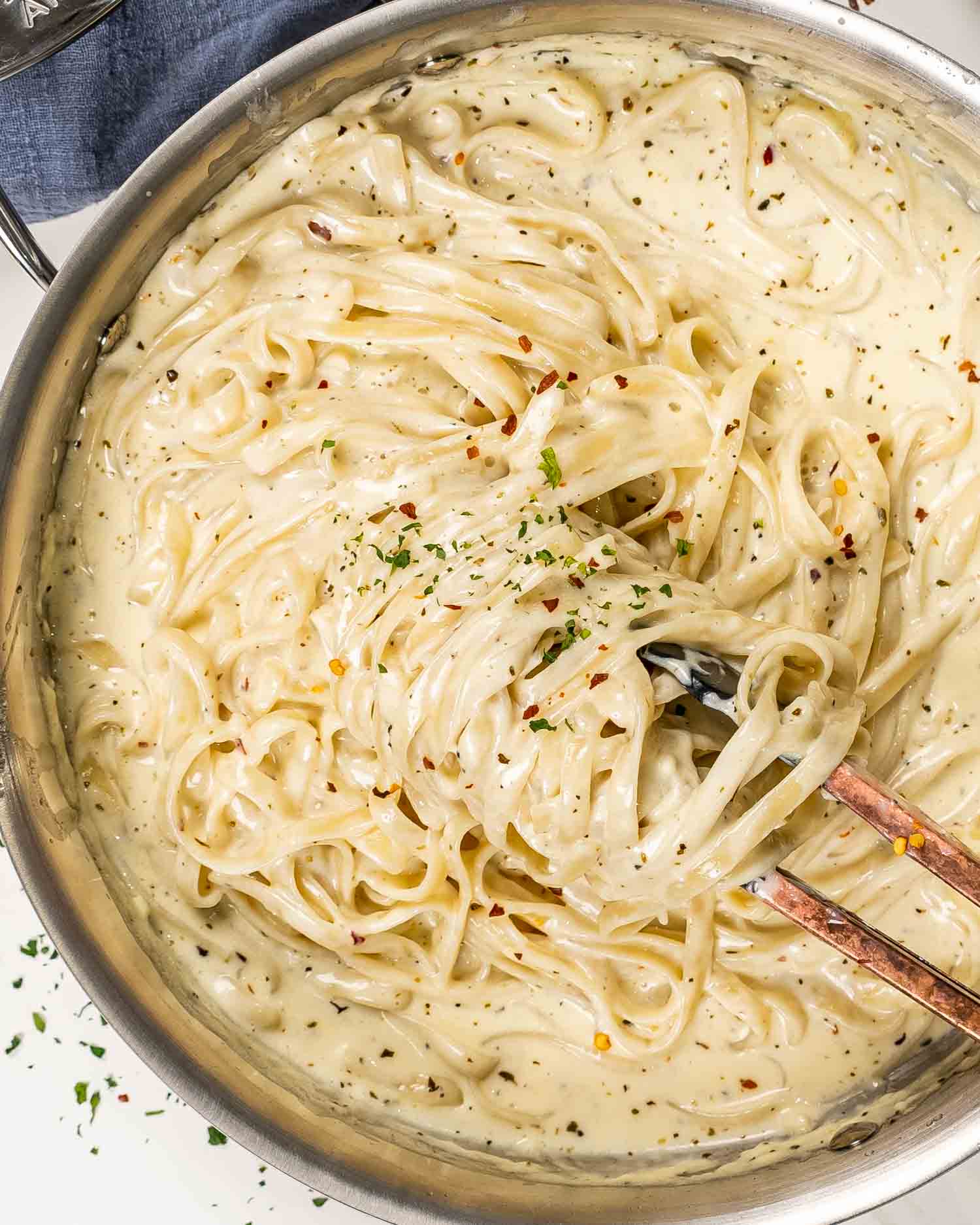 freshly made fettuccine alfredo in a skillet garnished with red pepper flakes and parsley.