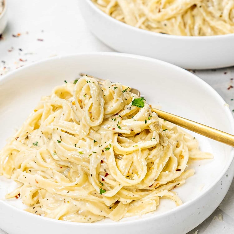 a serving of fettuccine alfredo in a white bowl with a golden fork.
