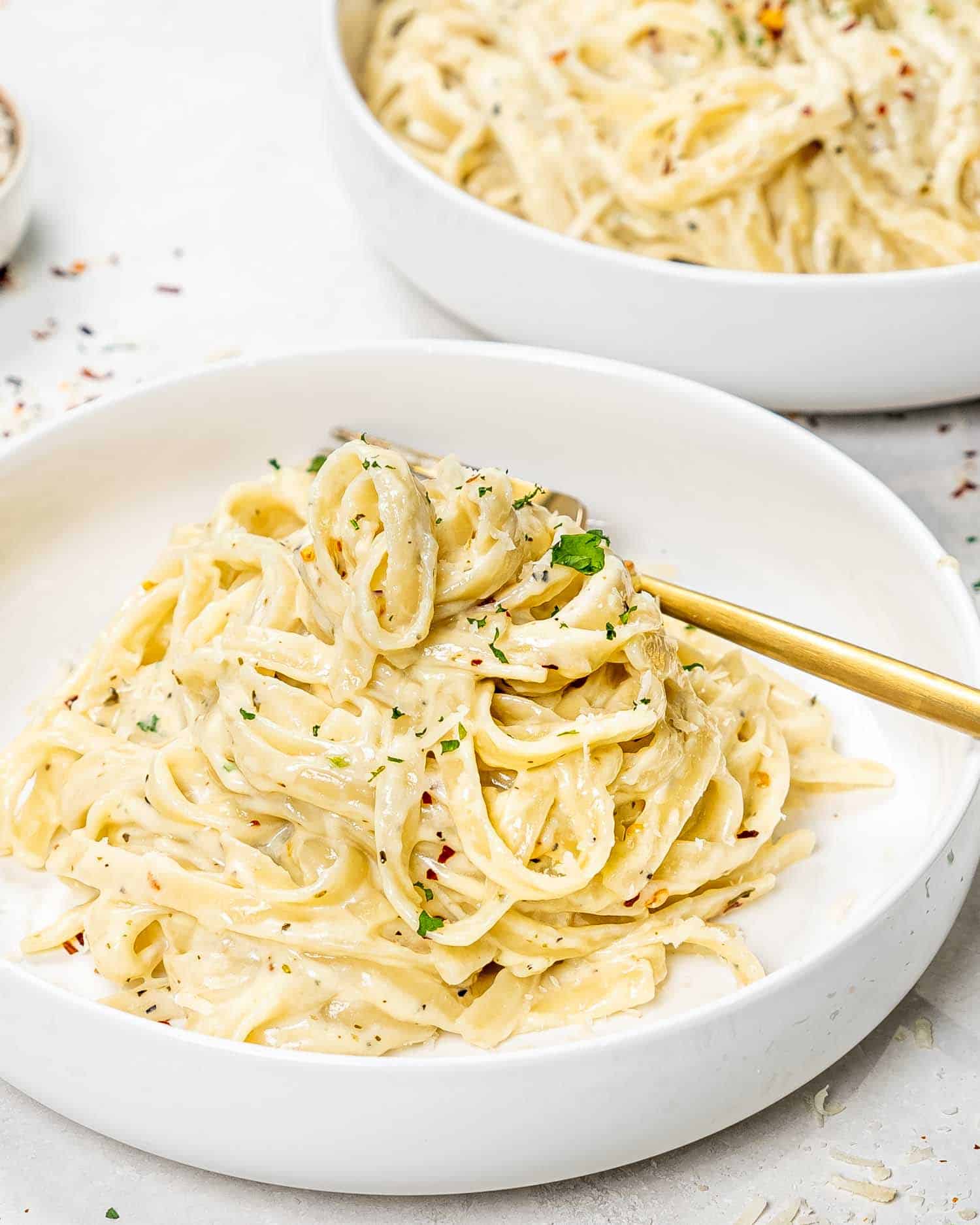 a serving of fettuccine alfredo in a white bowl with a golden fork.