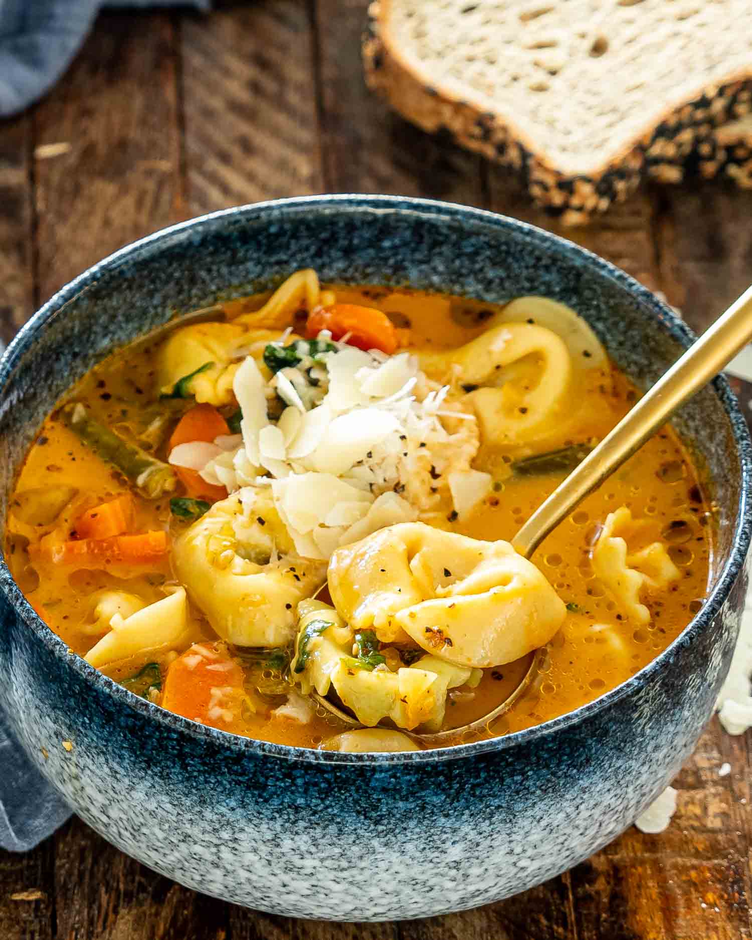 vegetable tortellini soup in a blue bowl garnished with parmesan cheese.