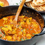 balti chicken garnished with cilantro in a black cast iron pot.