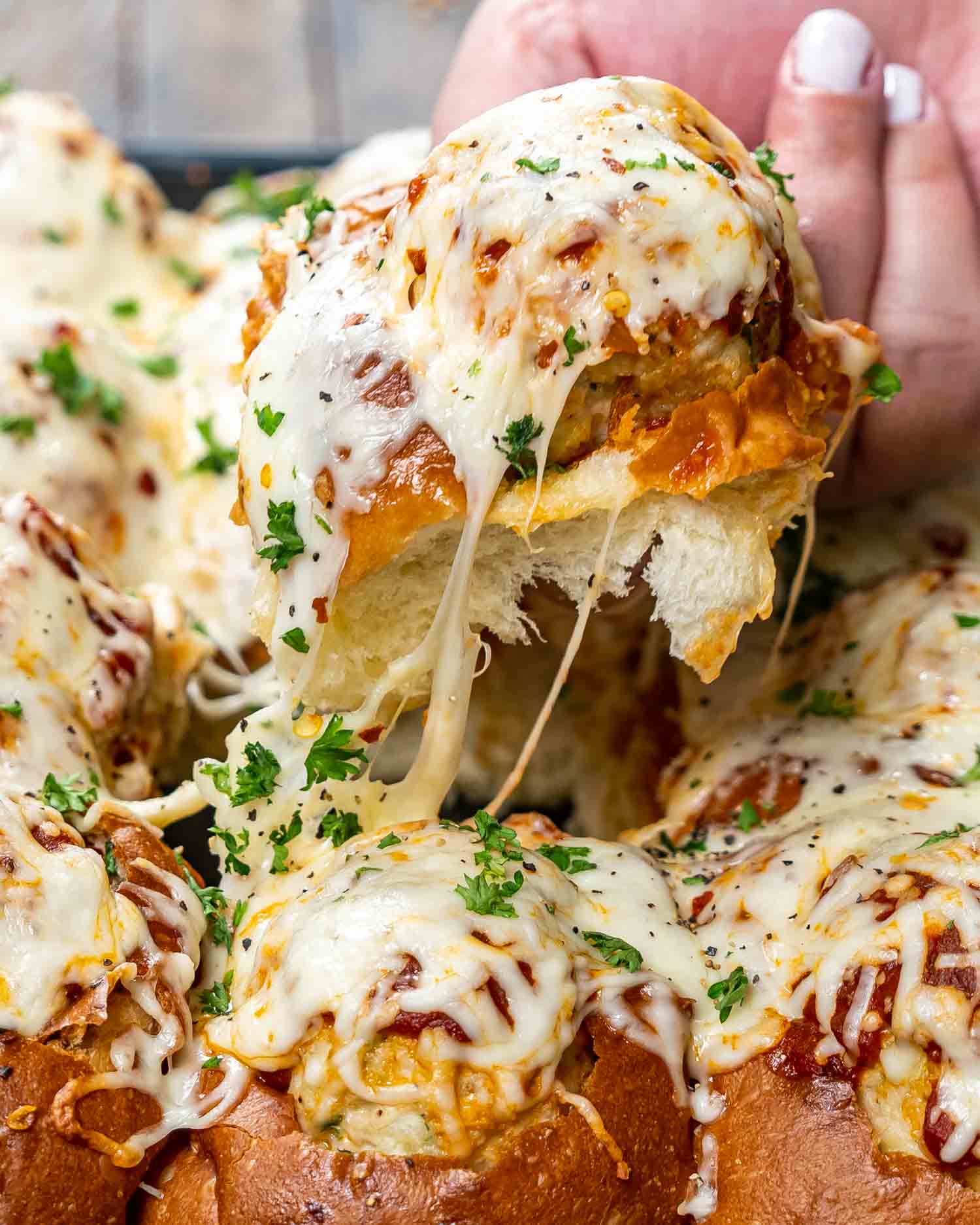 a hand pulling a meatball sliders from a baking sheet full of meatball sliders.