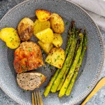 a mini turkey meatloaf on a plate with roasted potatoes and asparagus.