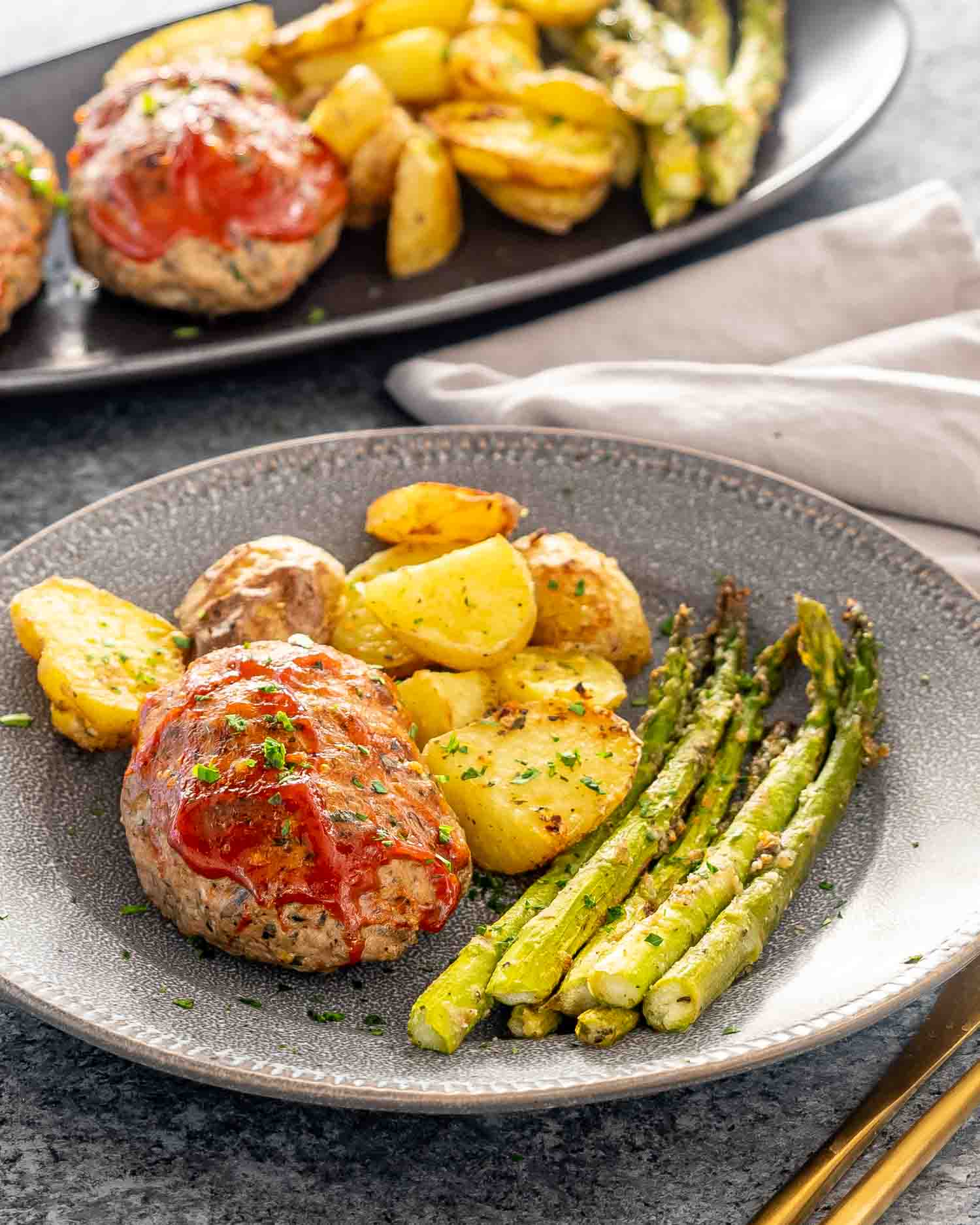 a mini turkey meatloaf on a plate with roasted potatoes and asparagus.