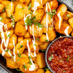 patatas bravas in an oval skillet with spicy red sauce.