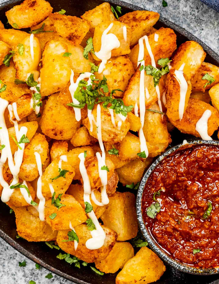 patatas bravas in an oval skillet with spicy red sauce.
