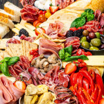 an antipasto platter loaded with salami, deli meats, mix of olives, cheeses, crackers and nuts.