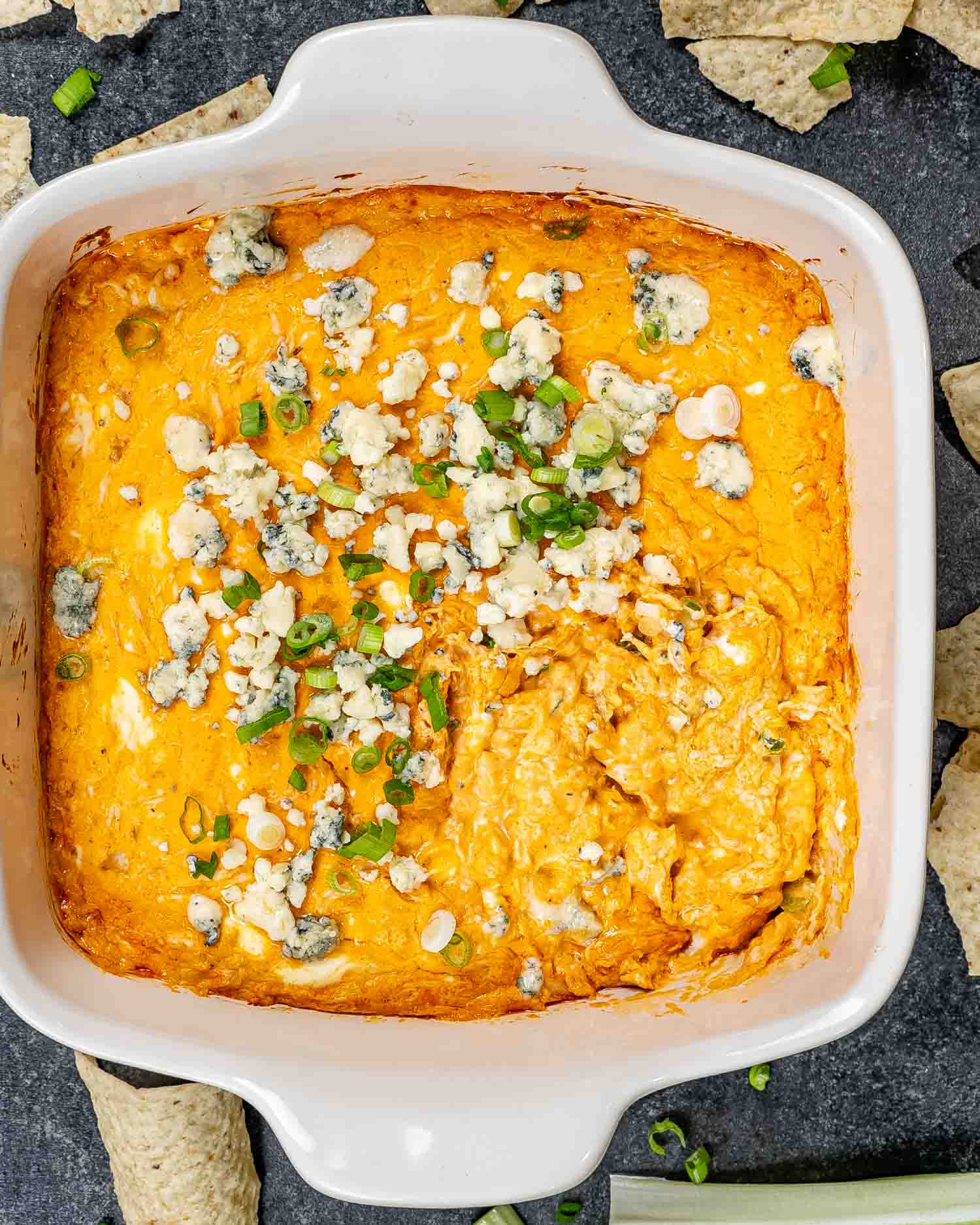 buffalo chicken dip in a square baking dish garnished with blue cheese and green onions.