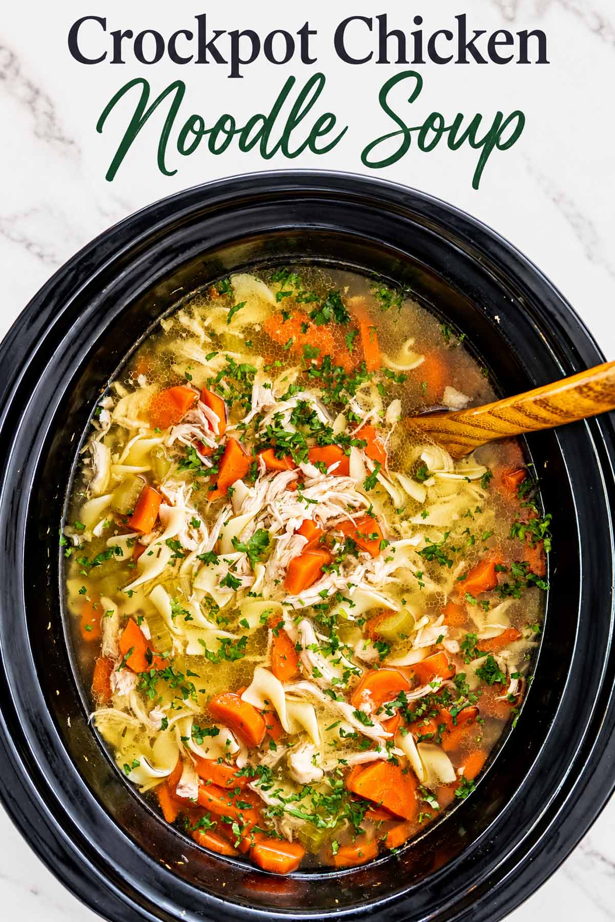Overhead crockpot chicken noodle soup with shredded chicken, carrots, celery and wide noodles beneath an elegant recipe title.