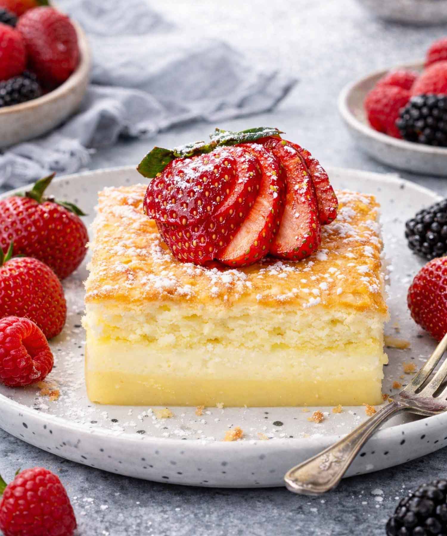 magic cake on a plate garnished with powdered sugar and a strawberry.
