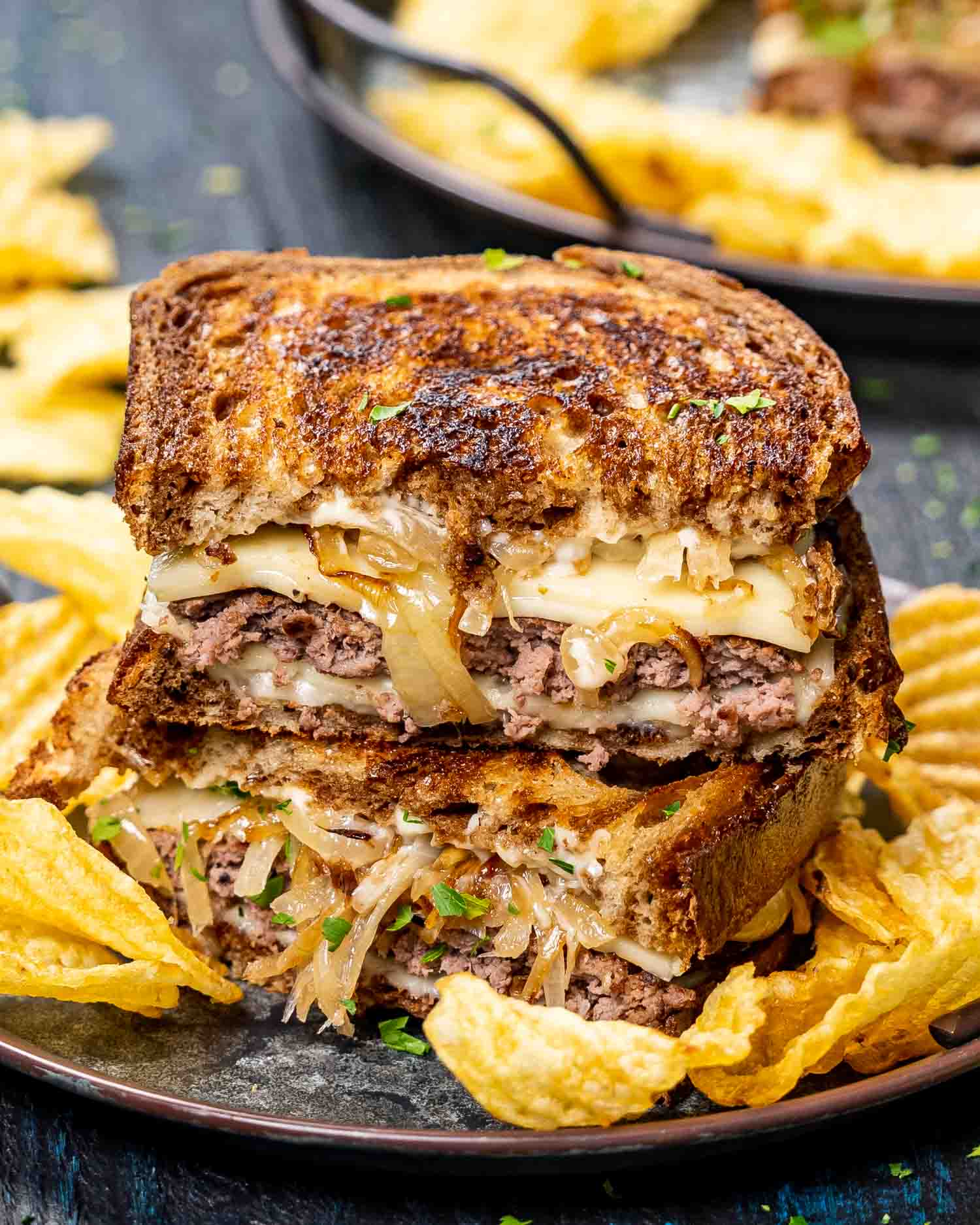 two patty melt sandwiches stacked with potato chips on a plate.