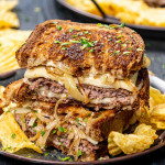 two patty melt sandwiches stacked with potato chips on a plate.