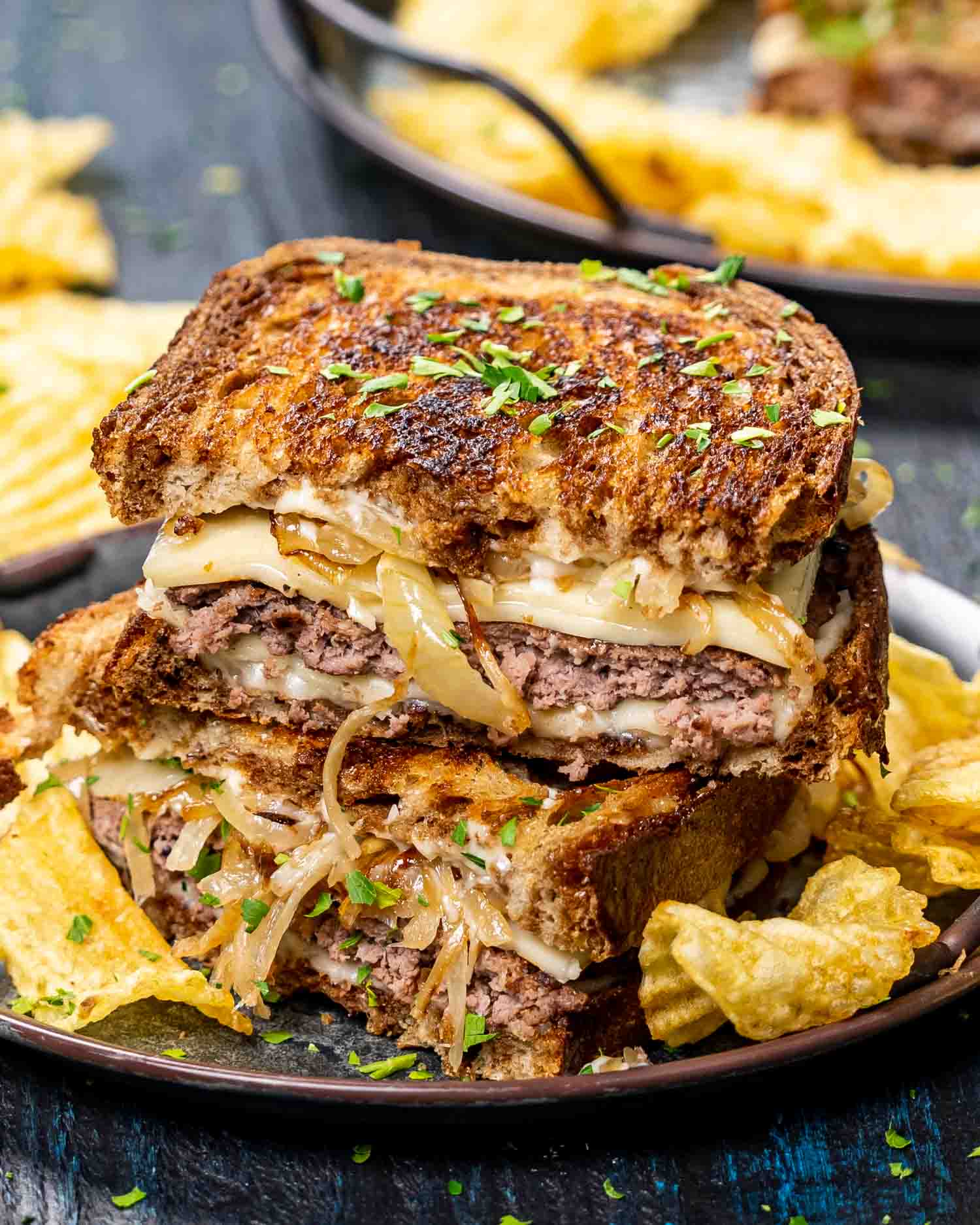 two patty melt sandwiches stacked with potato chips on a plate.