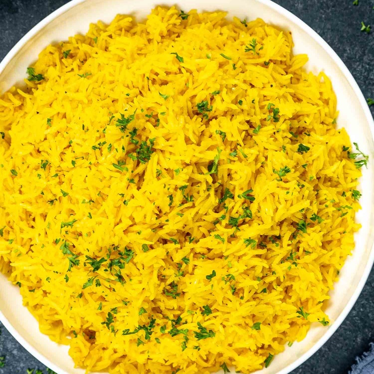 yellow rice in a white bowl garnished with parsley.