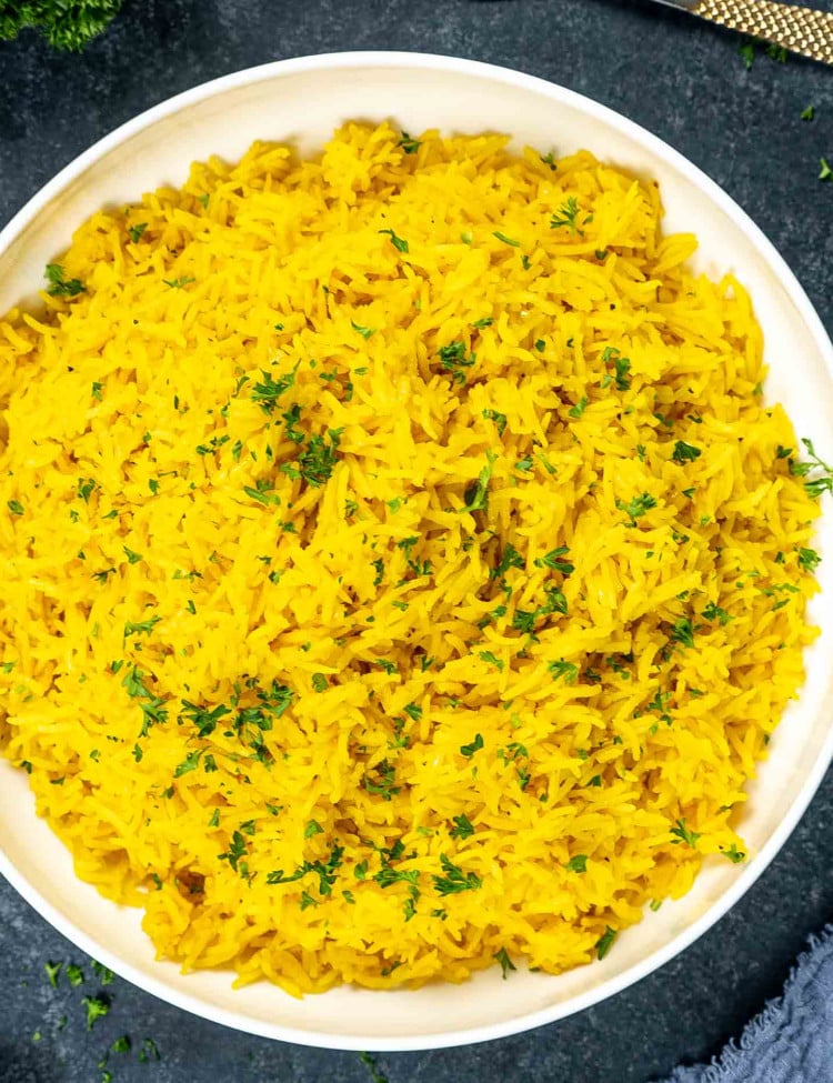 yellow rice in a white bowl garnished with parsley.