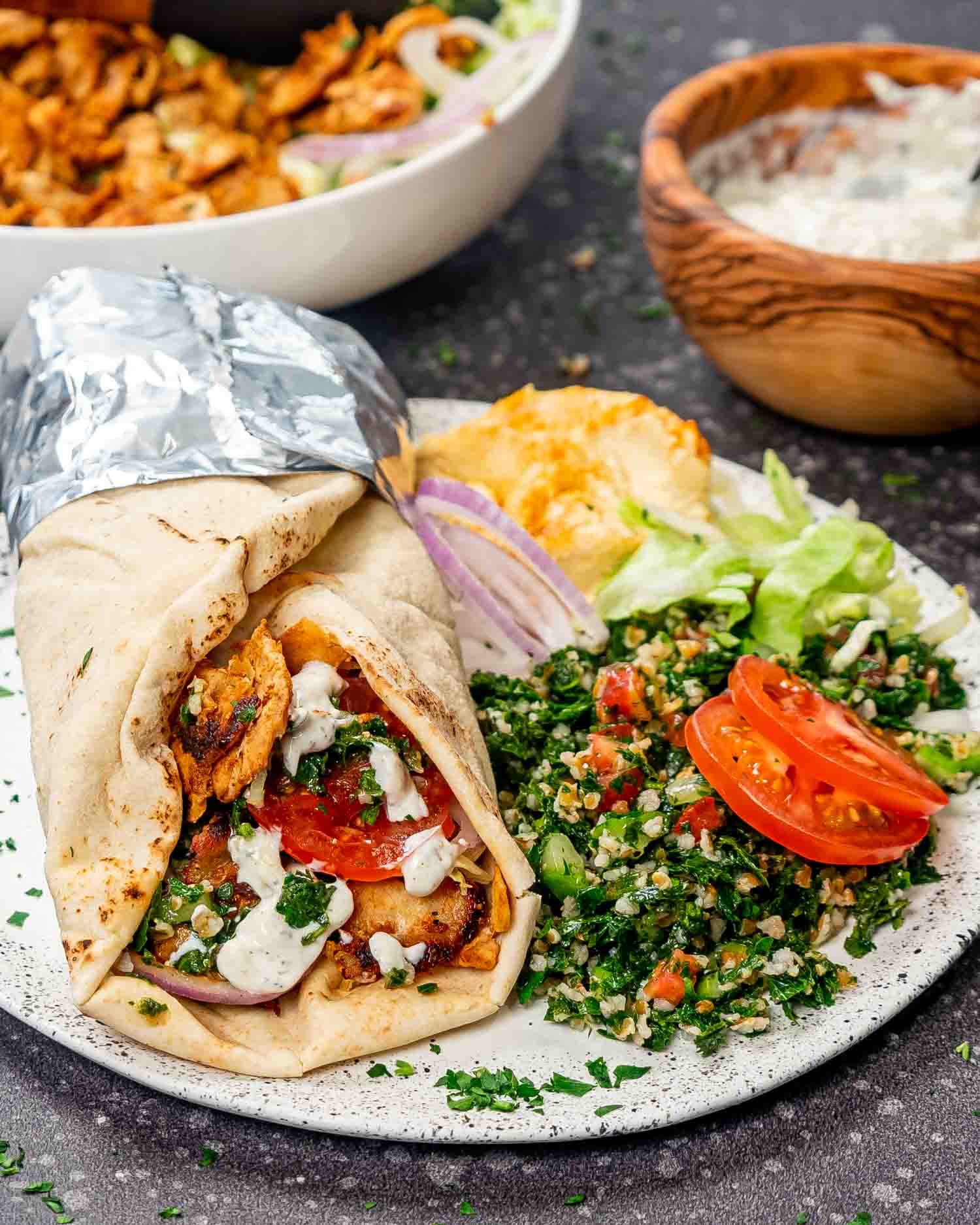 chicken doner kebabs on a cutting board with a delicious yogurt sauce and tabbouleh salad.