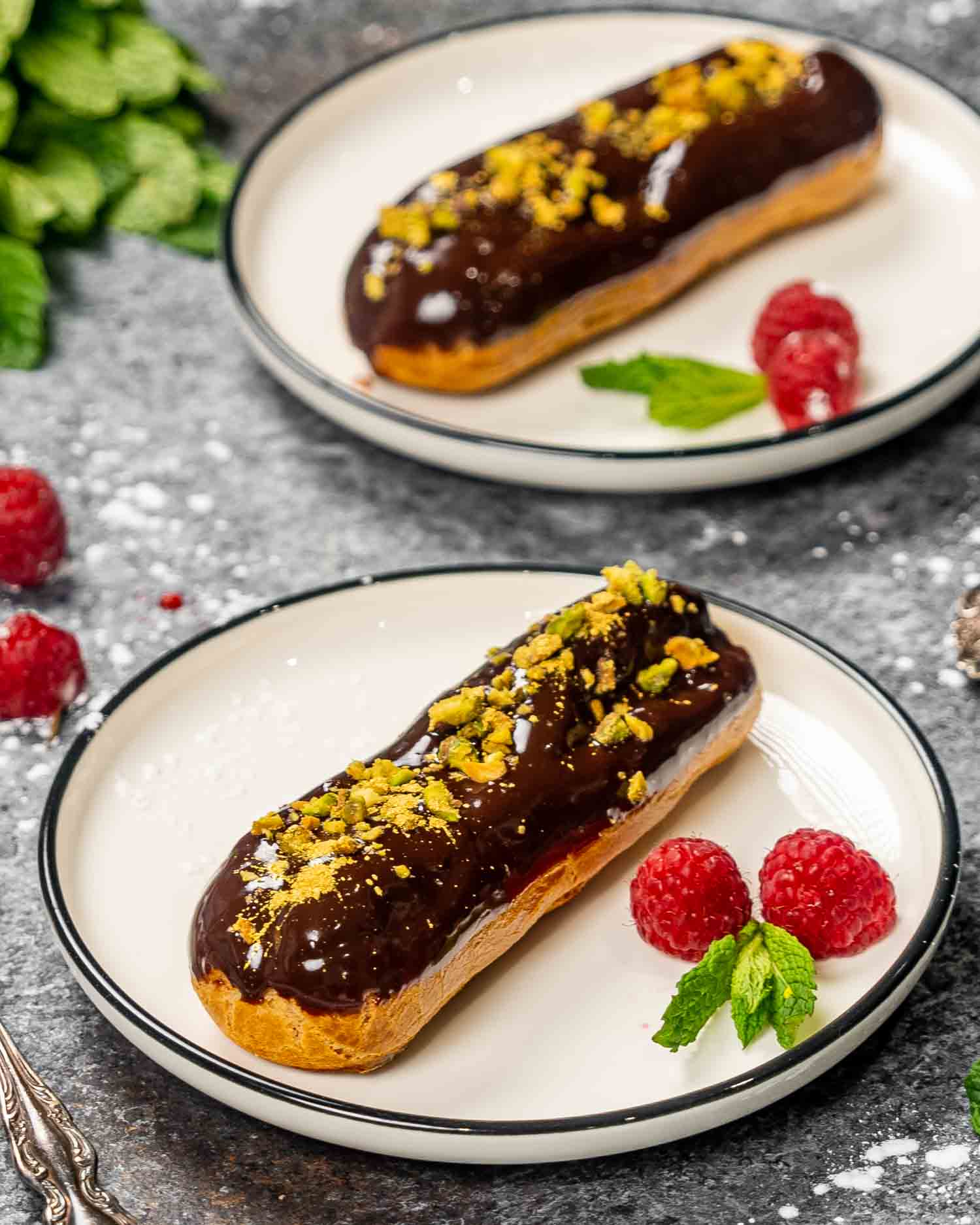 an eclair filled with pastry cream and dipped in chocolate and topped with pistachios.